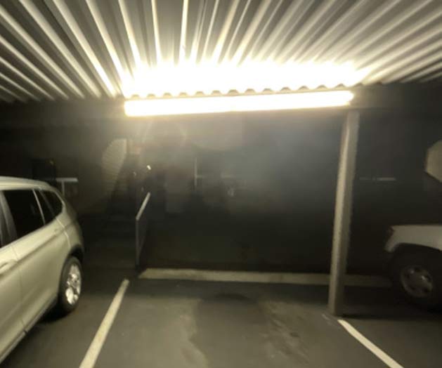 Lighting fixture mounted under a covered walkway overhang illuminating the ceiling rather than the pedestrian surface below