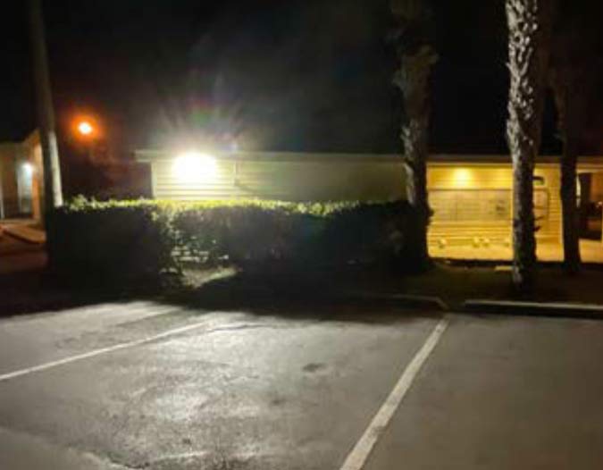 Flood light mounted at low elevation without a cutoff shield creating glare that blinds approaching pedestrians on a Florida multifamily property